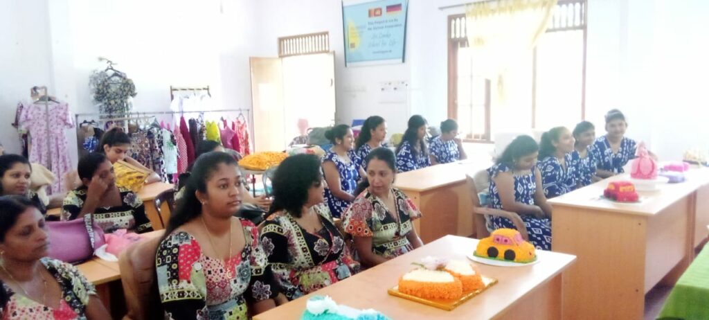 Alle Kursmitglieder zusammen in unserem Unterrichtsraum. Im Vordergrund die von den Schülerinnen gebackenen Torten und im Hintergrund die genähten Kleider.